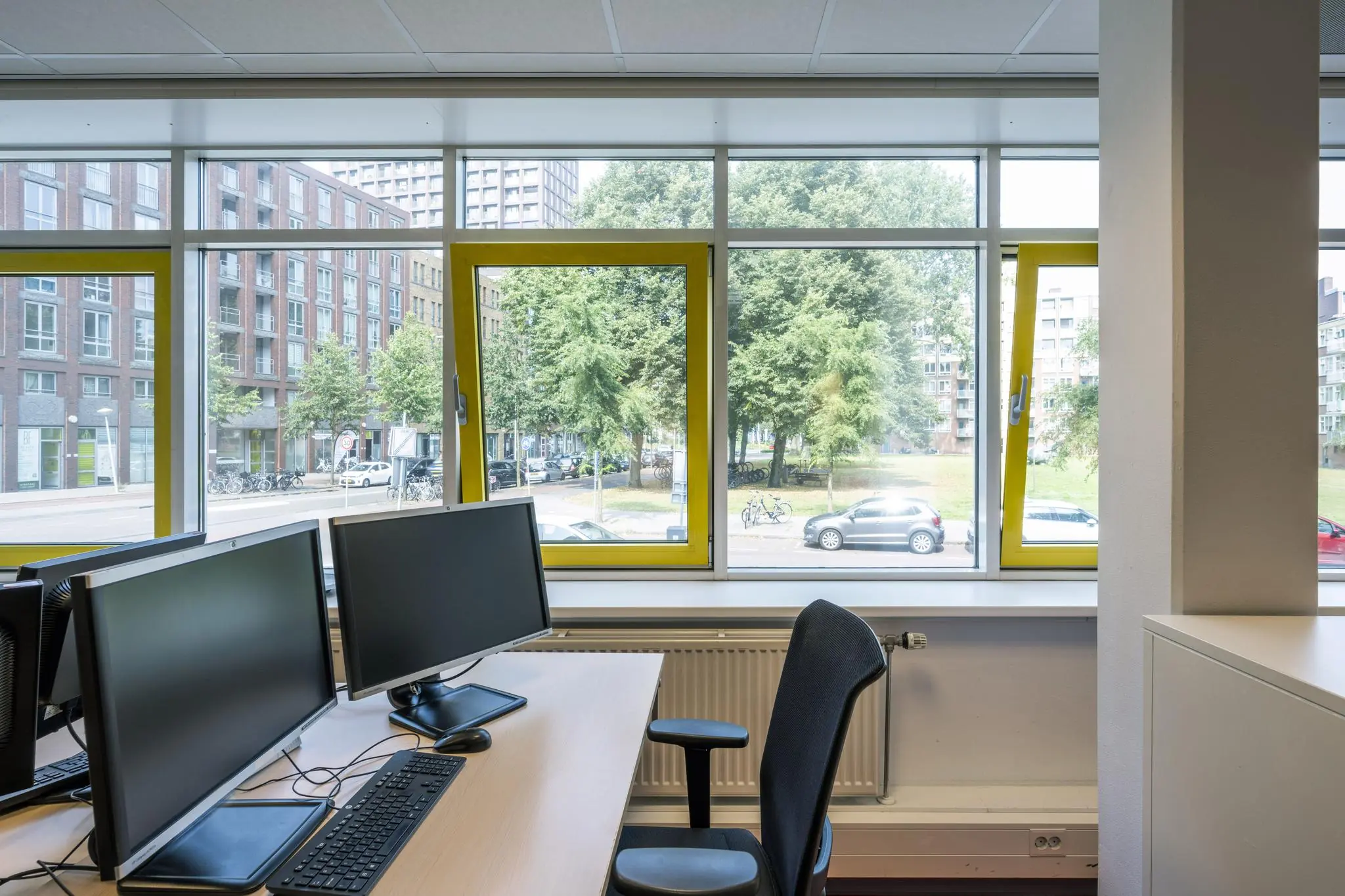 Moderne kantoorruimte aan de Jan Tooropstraat met bureaus, computerschermen en uitzicht op de straat en omliggende gebouwen.